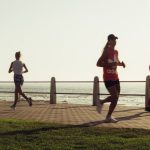 Full body of group women in activewear running and woman with dog walking on embankment and admiring sunset sky on resort