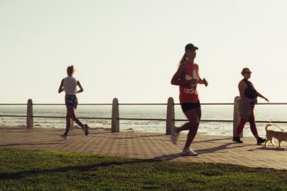 Full body of group women in activewear running and woman with dog walking on embankment and admiring sunset sky on resort
