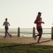 Full body of group women in activewear running and woman with dog walking on embankment and admiring sunset sky on resort